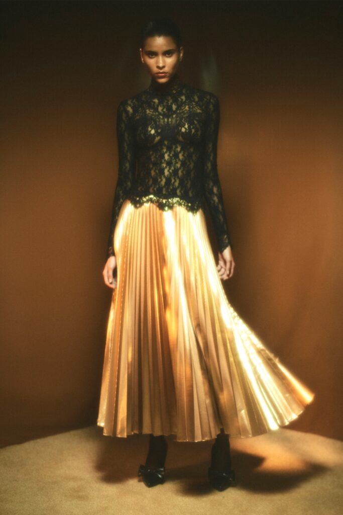 A fitted black lace dress with long sleeves and a pleated gold skirt.