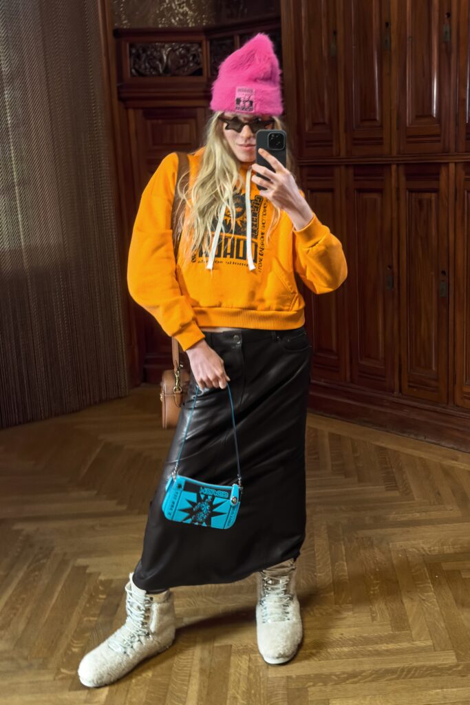 A relaxed black leather skirt paired with a hooded orange hoodie featuring an asymmetric design.