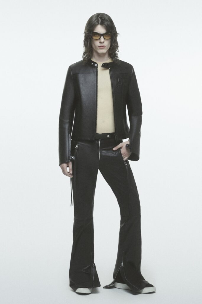 A fitted black leather jacket with long sleeves and flared pants featuring zippered details.