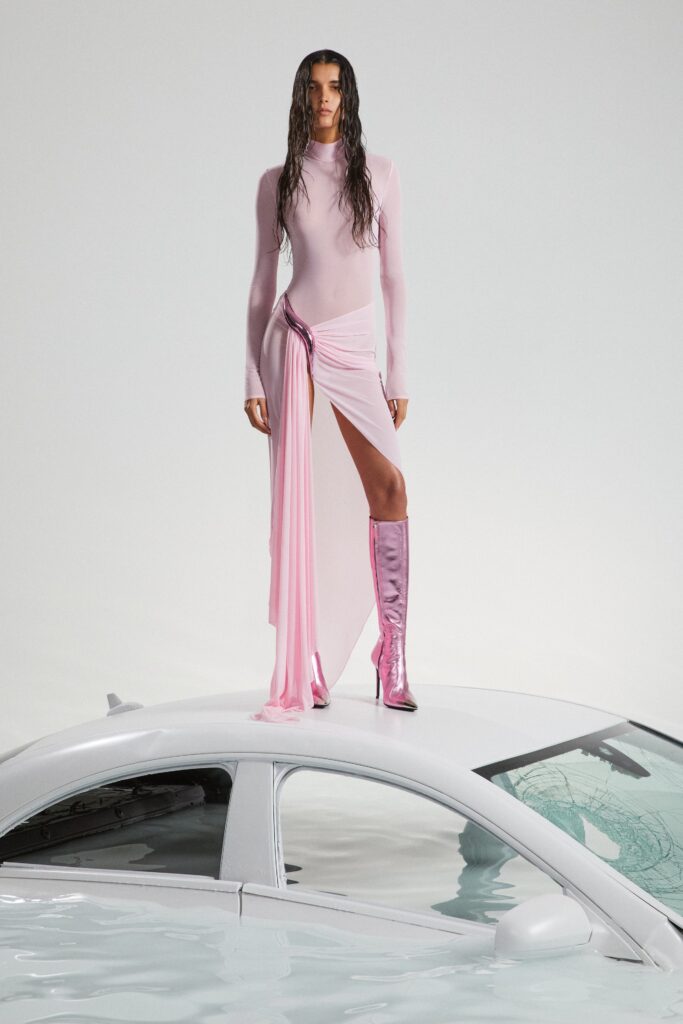 A fitted pink silk dress with long sleeves and an asymmetric draped design.