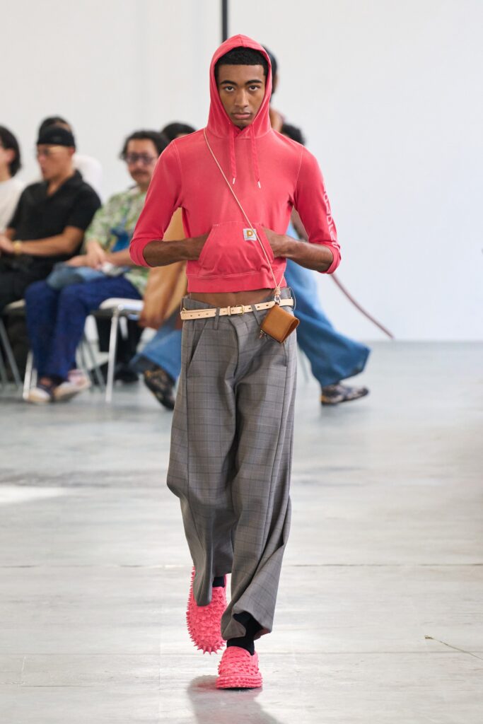 A relaxed pink hoodie with a hood paired with checked wide-leg gray pants.