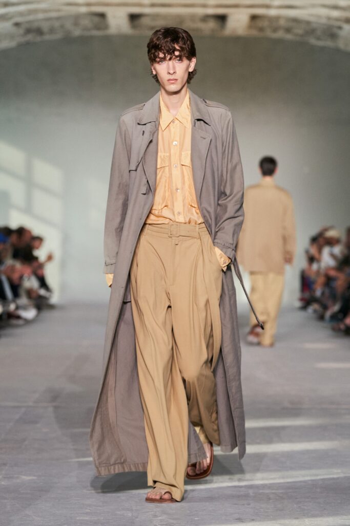 A relaxed beige trench coat layered over a collared long-sleeve orange shirt.