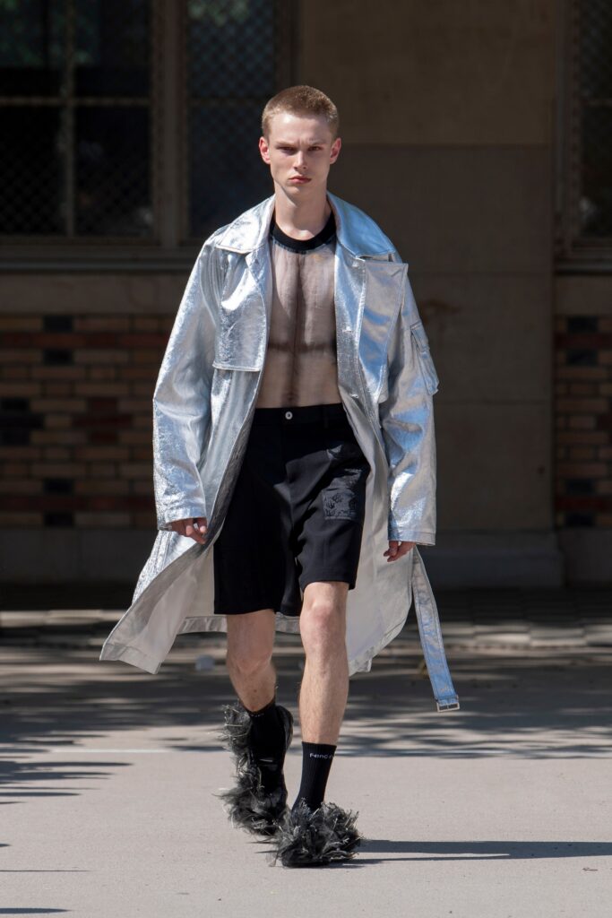 A relaxed silver metallic coat paired with black shorts featuring a zippered front and sheer detailing.