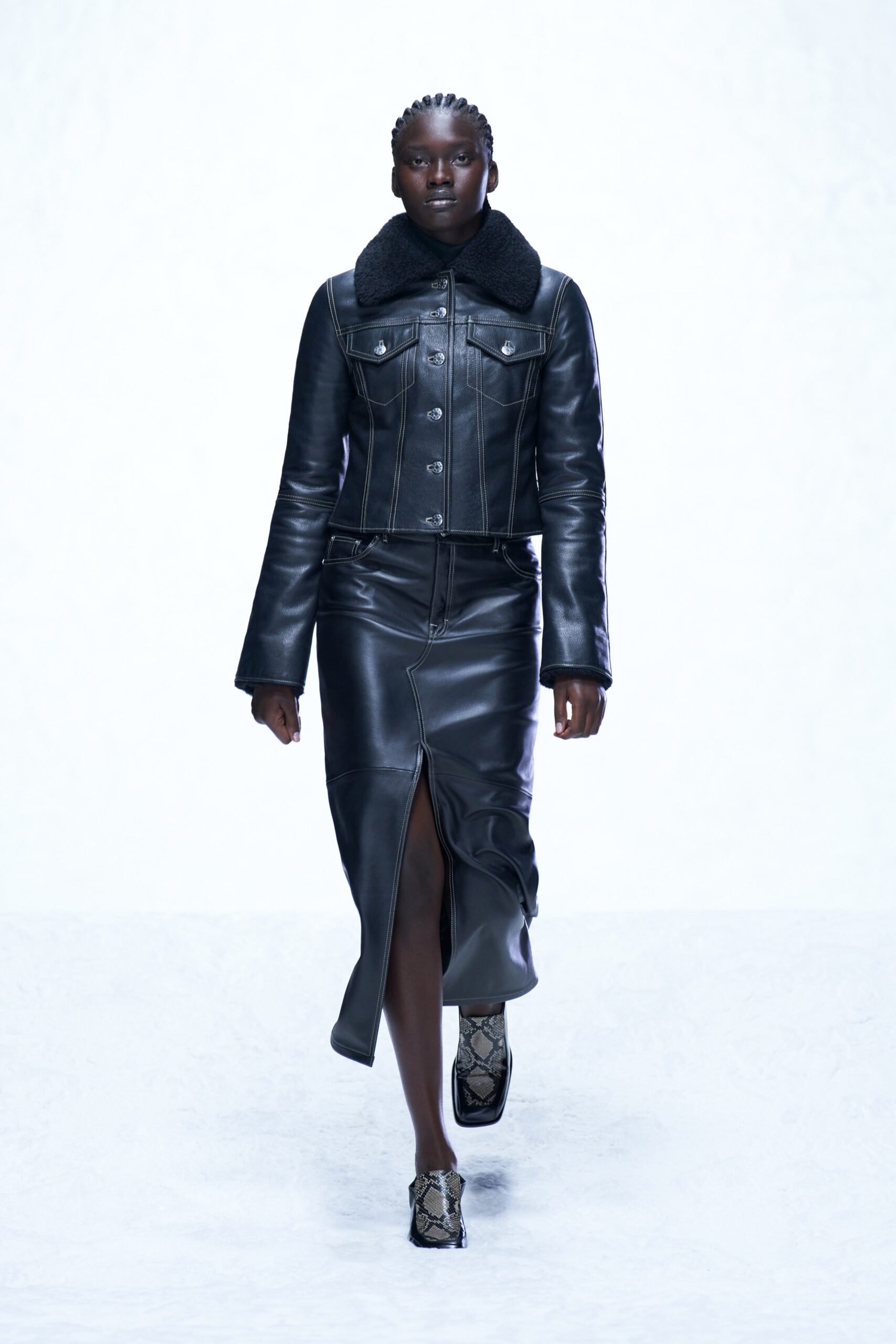 A fitted black leather jacket with a collared neckline paired with a fitted leather skirt featuring a slit.
