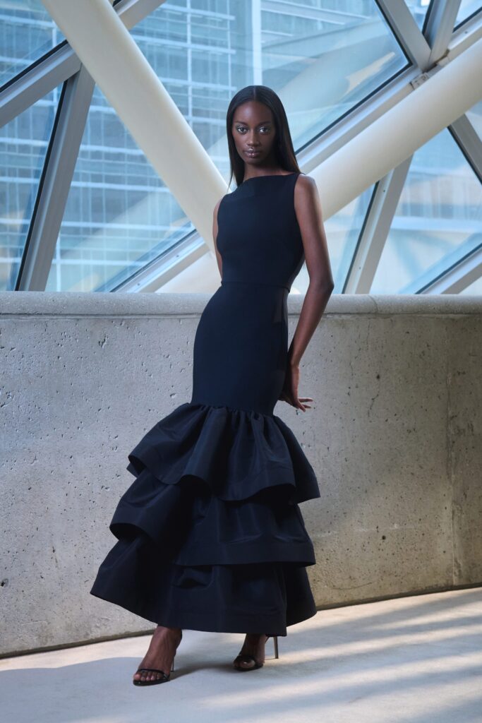 A fitted black sleeveless dress with a high neckline and tiered ruffles at the hem.