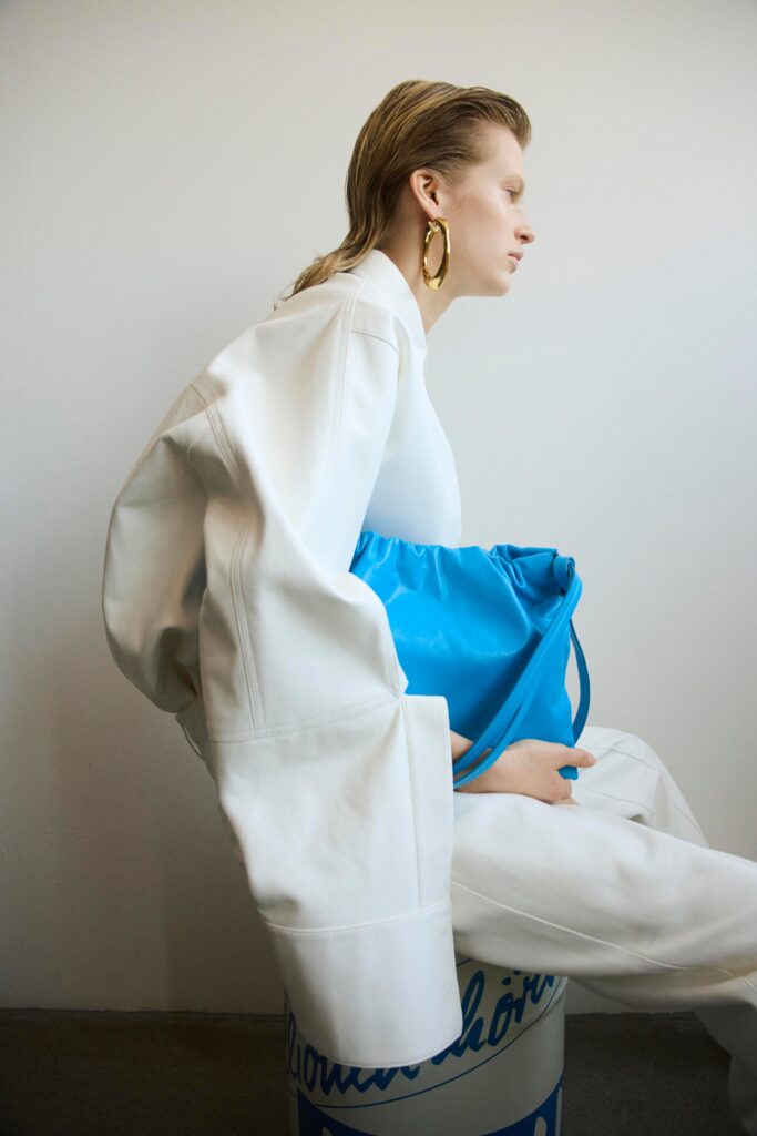 An oversized white leather jacket paired with blue pants, featuring a collared design and asymmetric details.