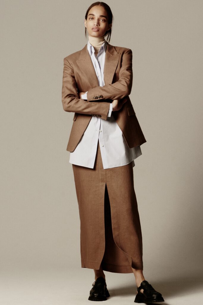A fitted brown linen blazer paired with a white collared shirt and a long skirt featuring a slit.