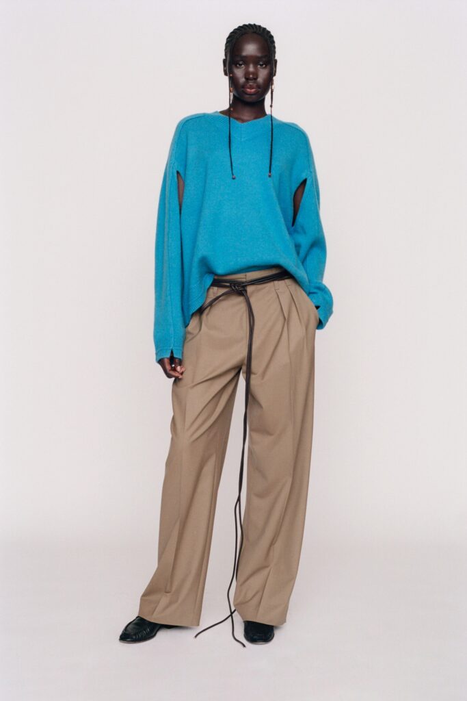 An oversized blue sweater with cutouts paired with wide-leg beige pants.