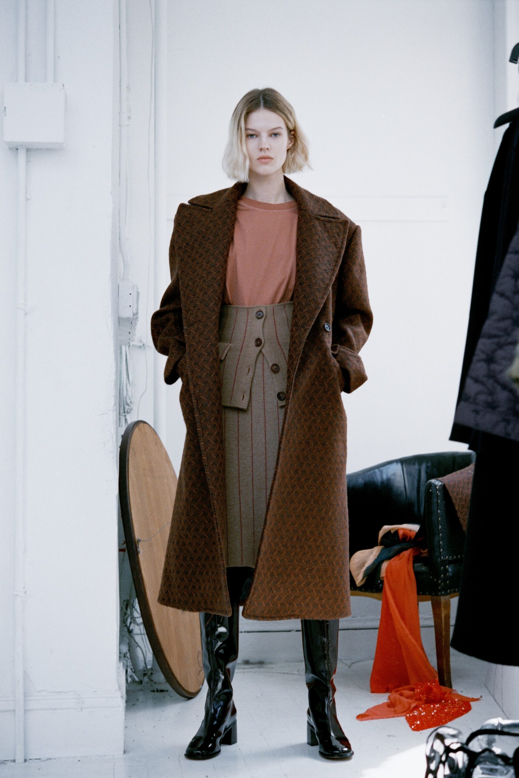 A fitted brown wool coat paired with a beige striped skirt and long-sleeve top.