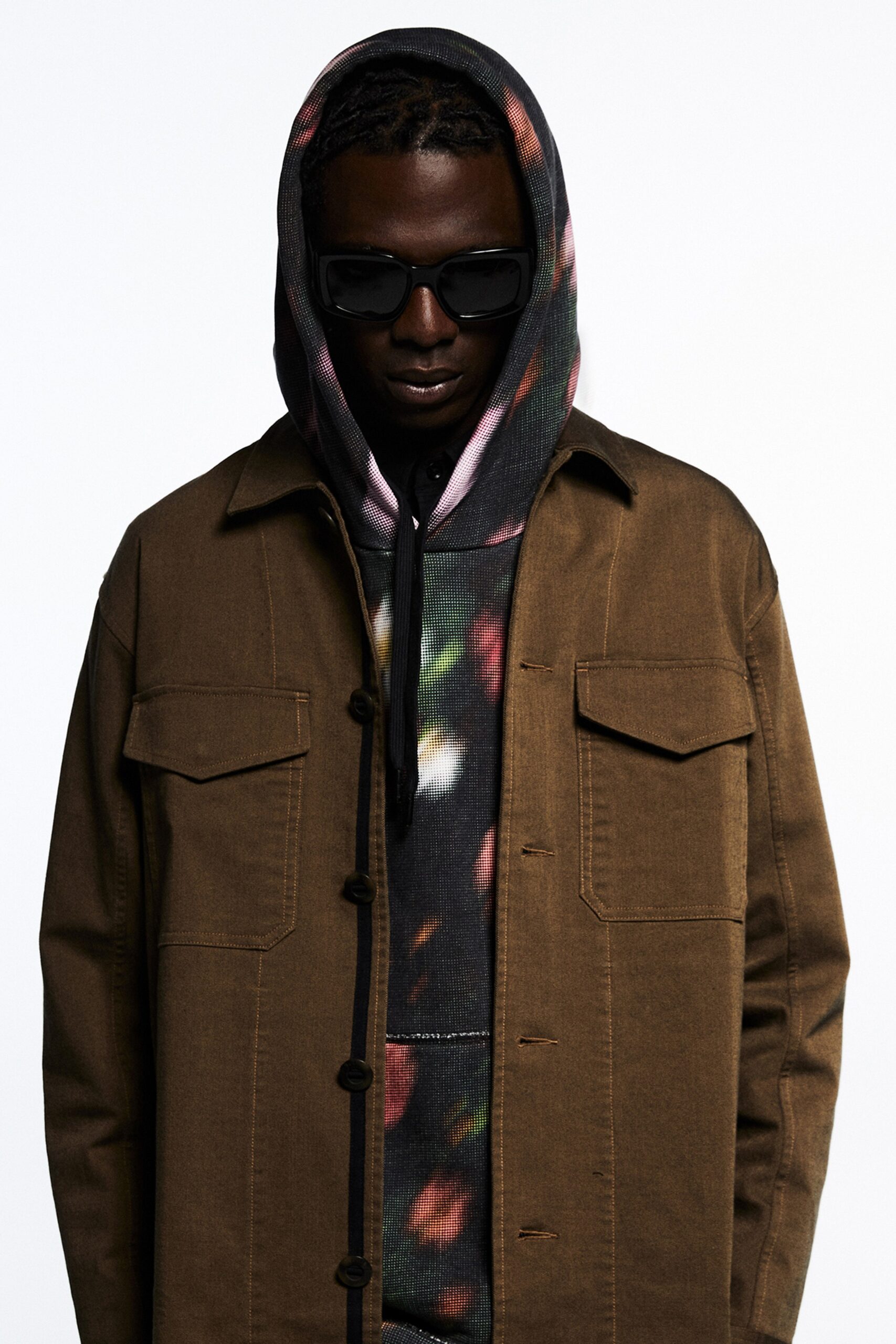 A relaxed brown jacket layered over a black hooded sweatshirt, featuring long sleeves and buttoned details.