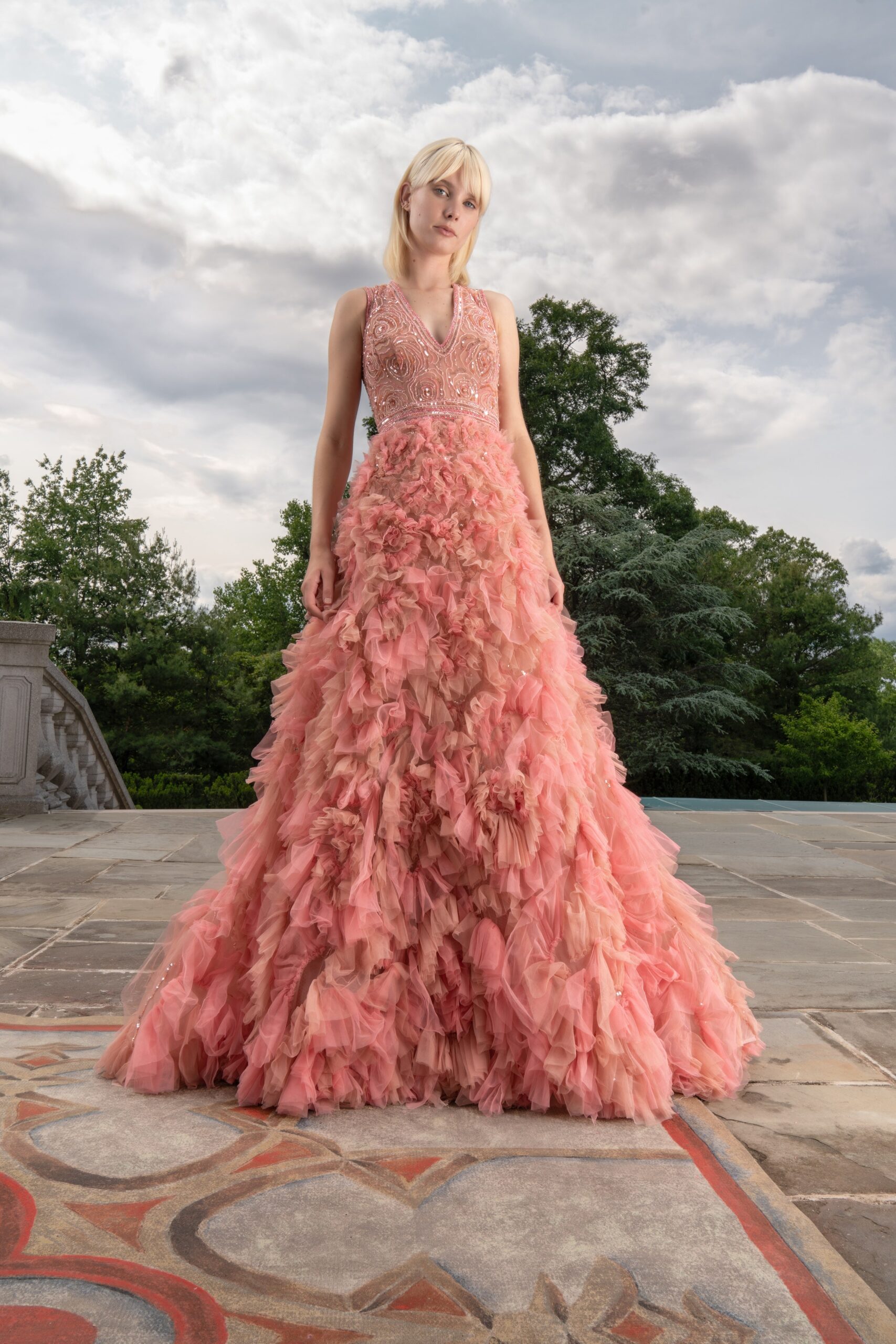A fitted pink tulle sleeveless gown with a V-neckline and tiered design.