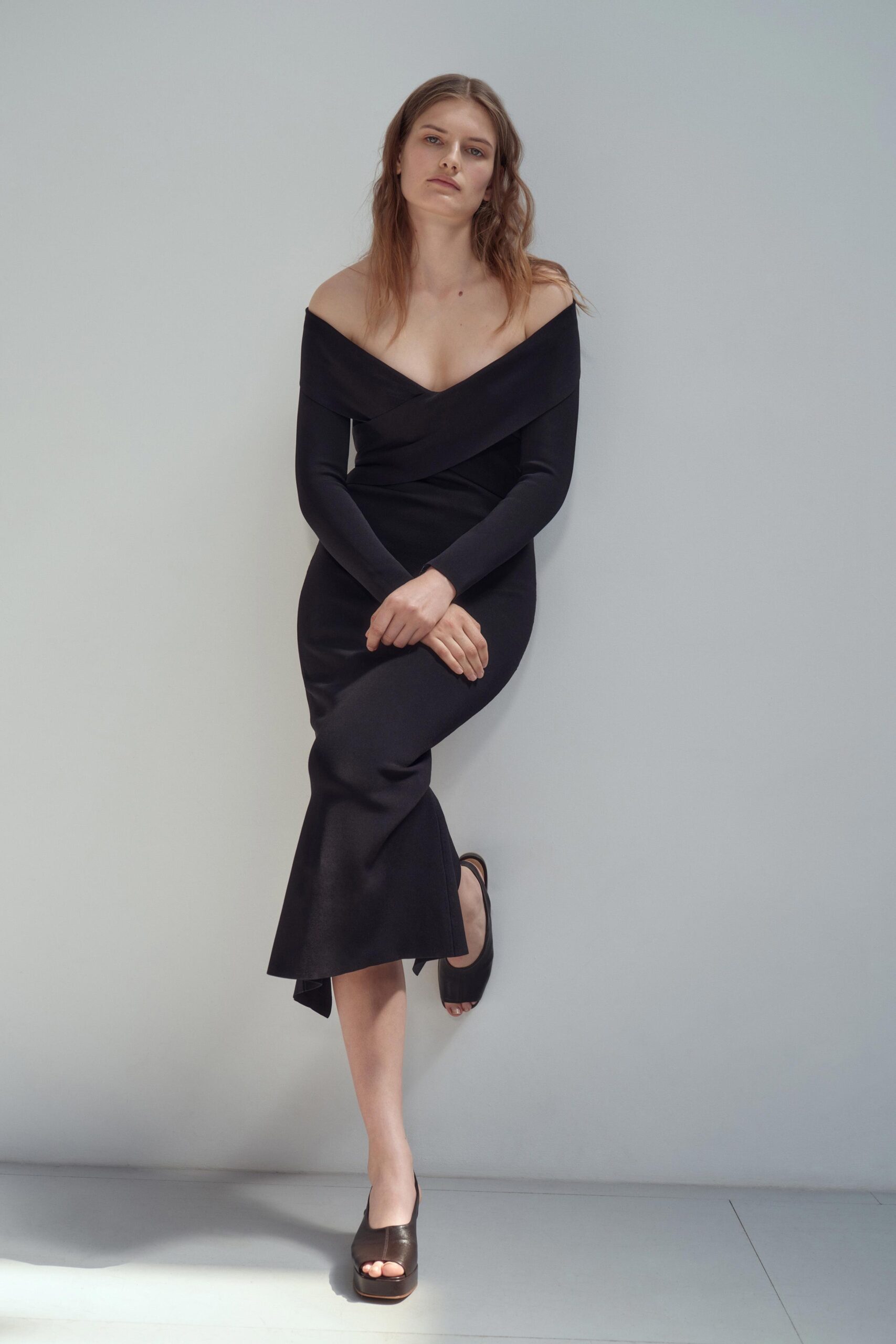 A fitted black dress with long sleeves and an off-shoulder design featuring a slit.