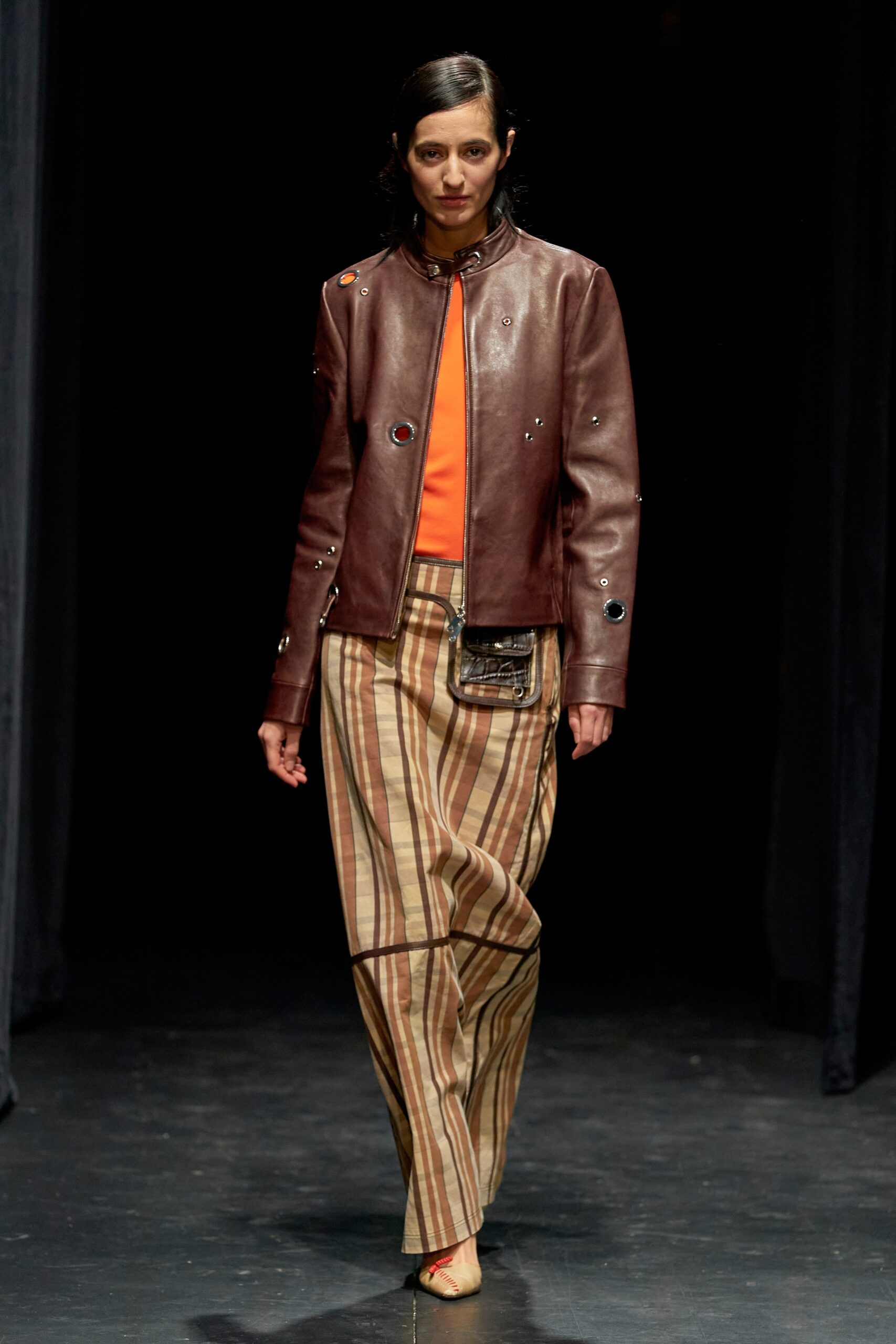 A relaxed brown leather jacket paired with striped cotton pants for a stylish runway look.