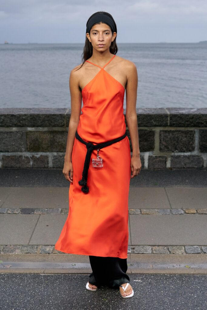 A fitted orange silk sleeveless dress with a V-neckline and asymmetric design.