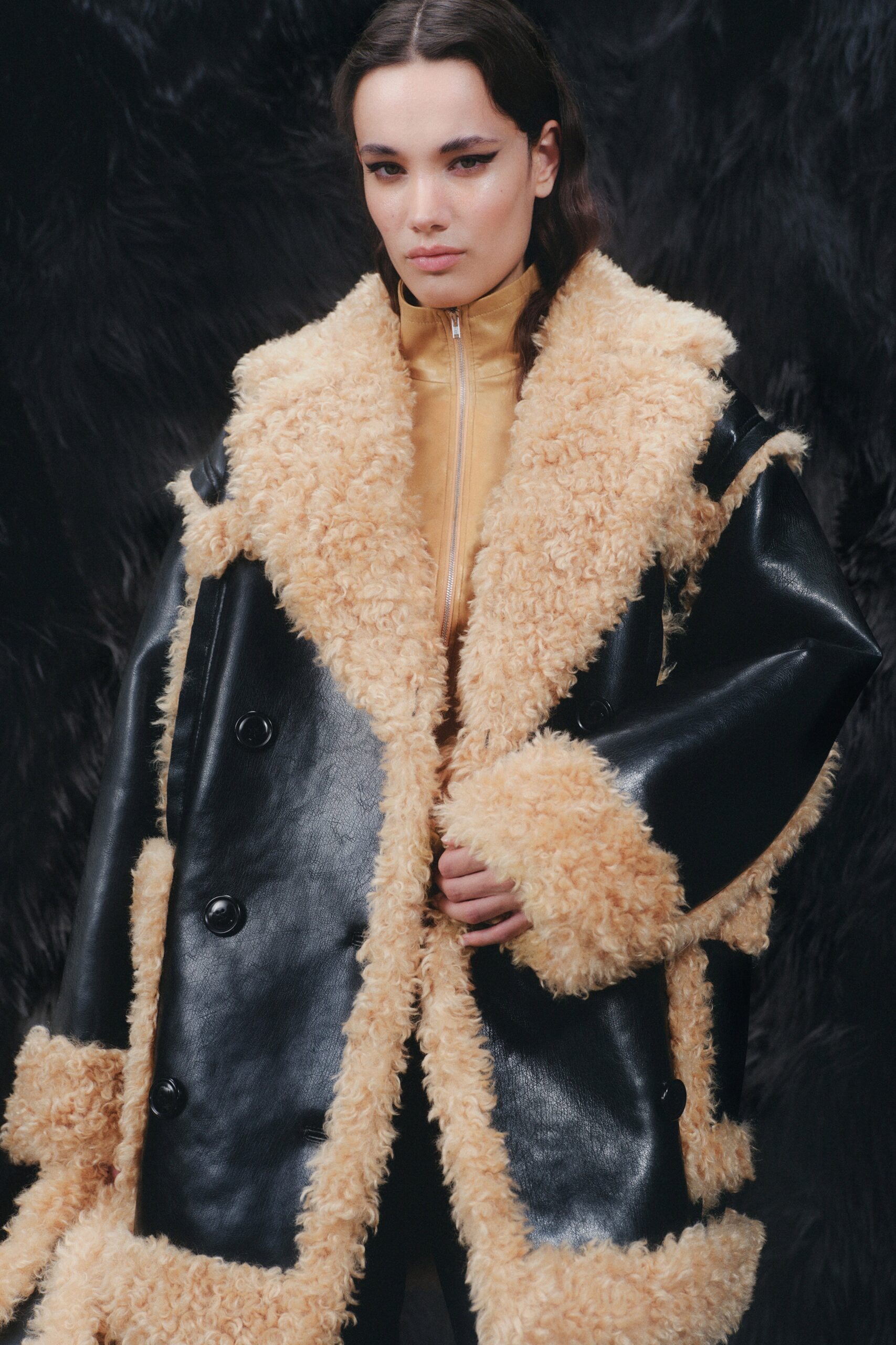 An oversized black and beige coat made of leather and fur with long sleeves and a collared design.