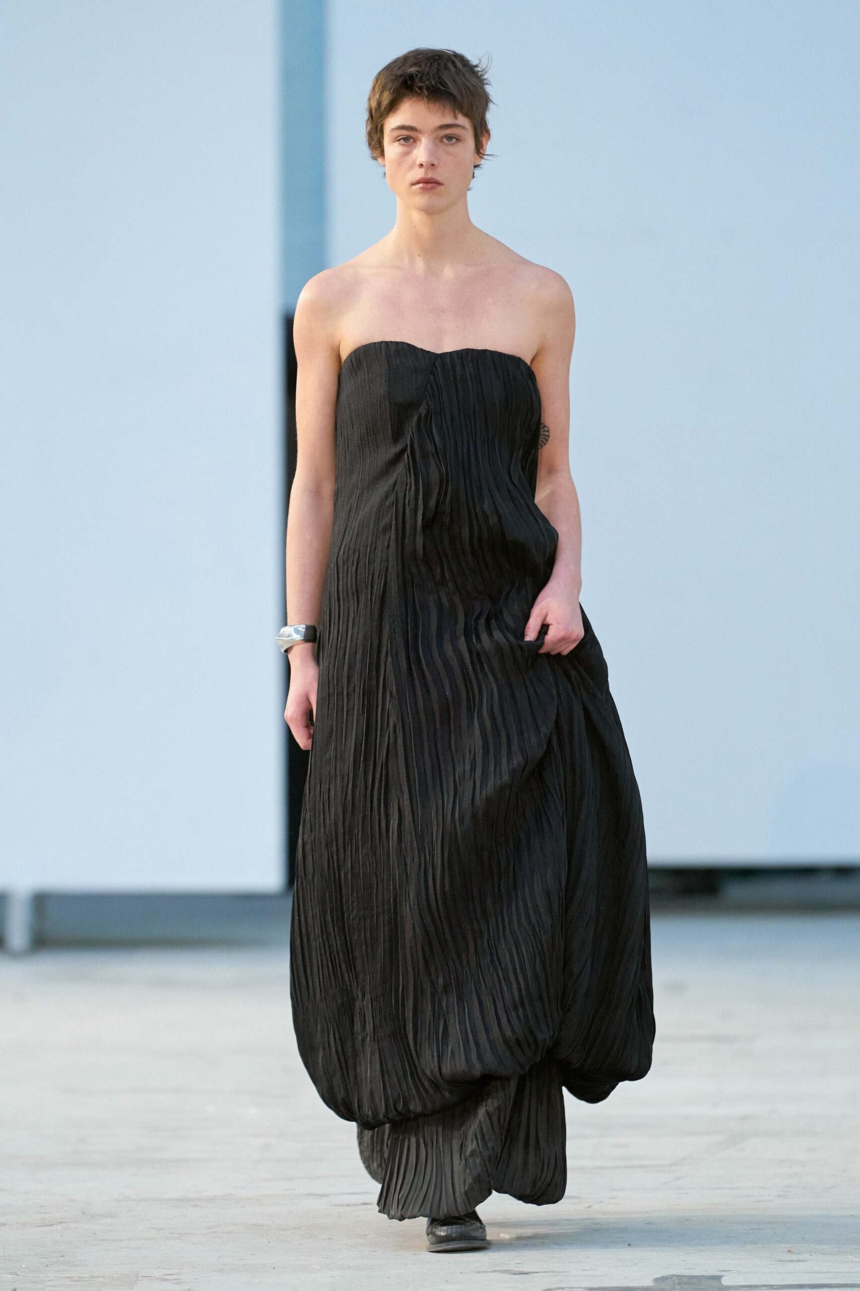 A relaxed black silk strapless dress featuring a pleated design for a flowing silhouette.