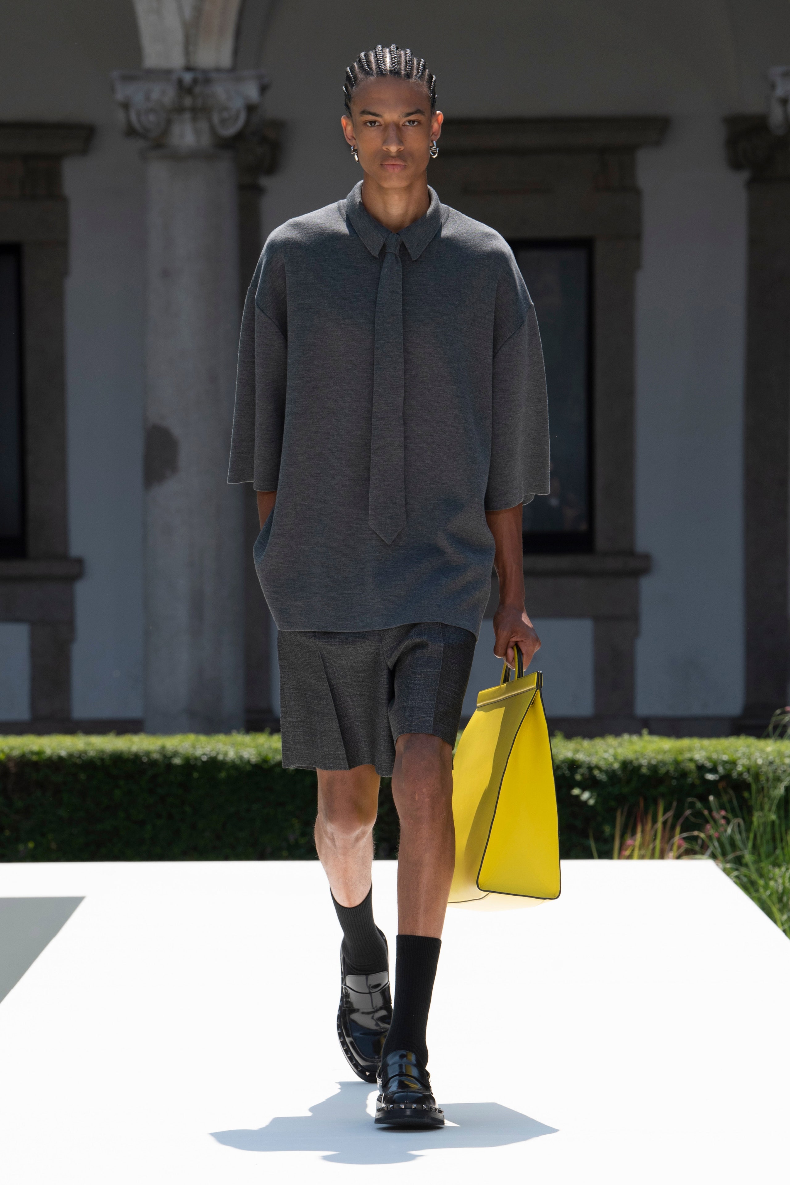 A relaxed gray shirt with a collared neckline paired with pleated black shorts.