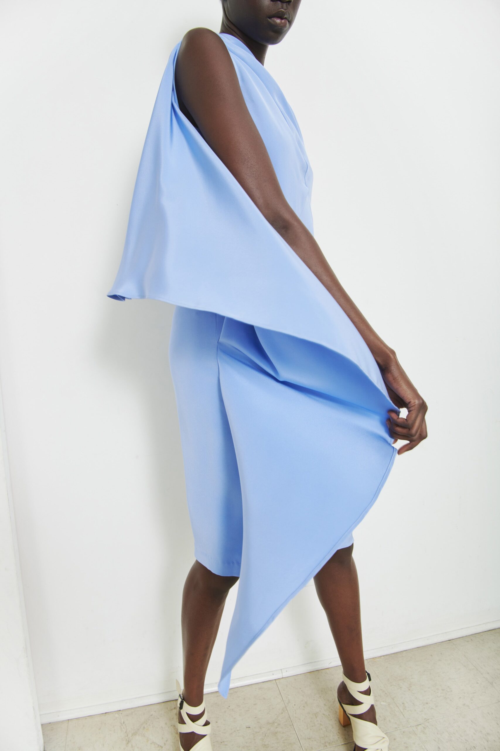 A fitted blue silk sleeveless dress with a high neckline and asymmetric design detail.