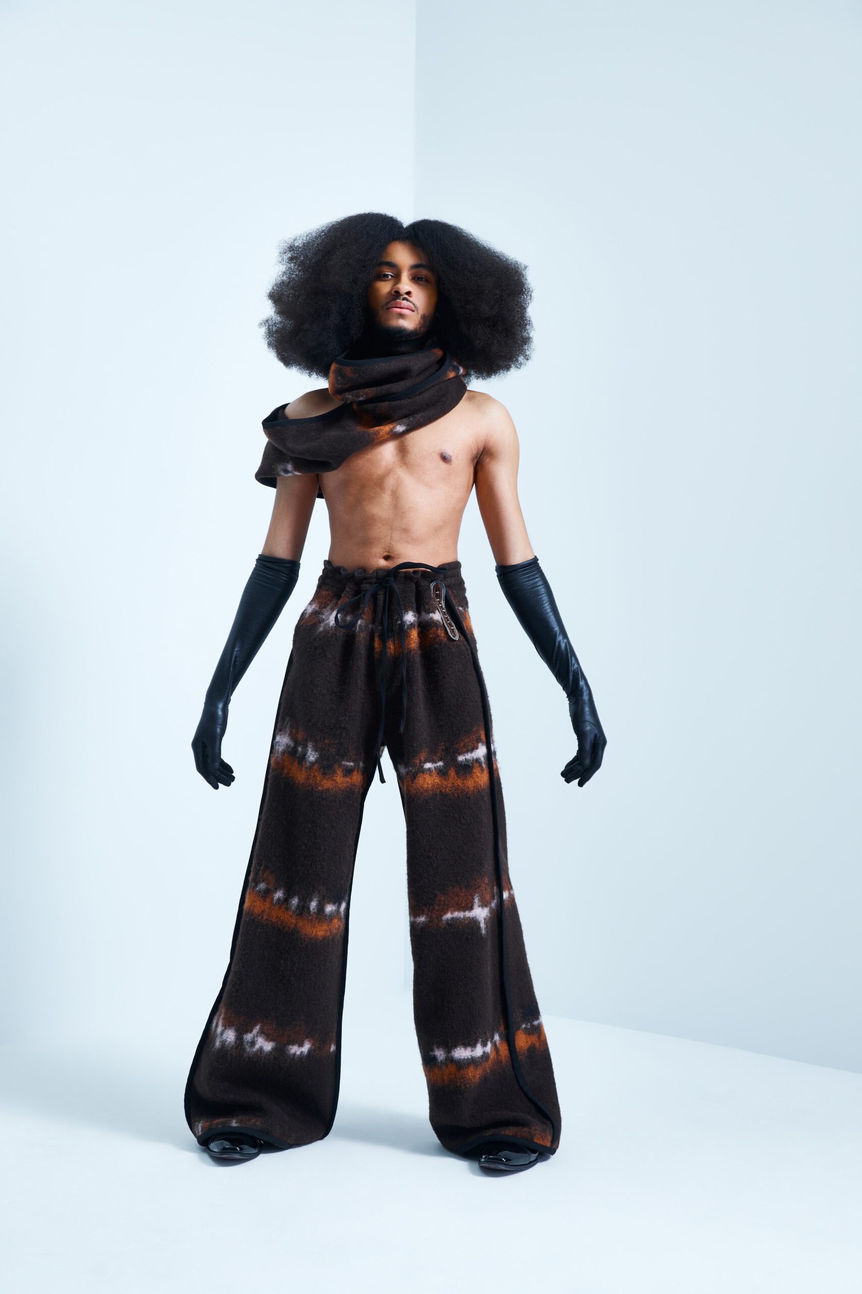 This ensemble features relaxed pants paired with a sleeveless top, both showcasing a unique tie-dye pattern in rich brown and black hues. The flared silhouette of the pants adds a dramatic flair, while the high-neck construction of the top creates a striking visual balance.