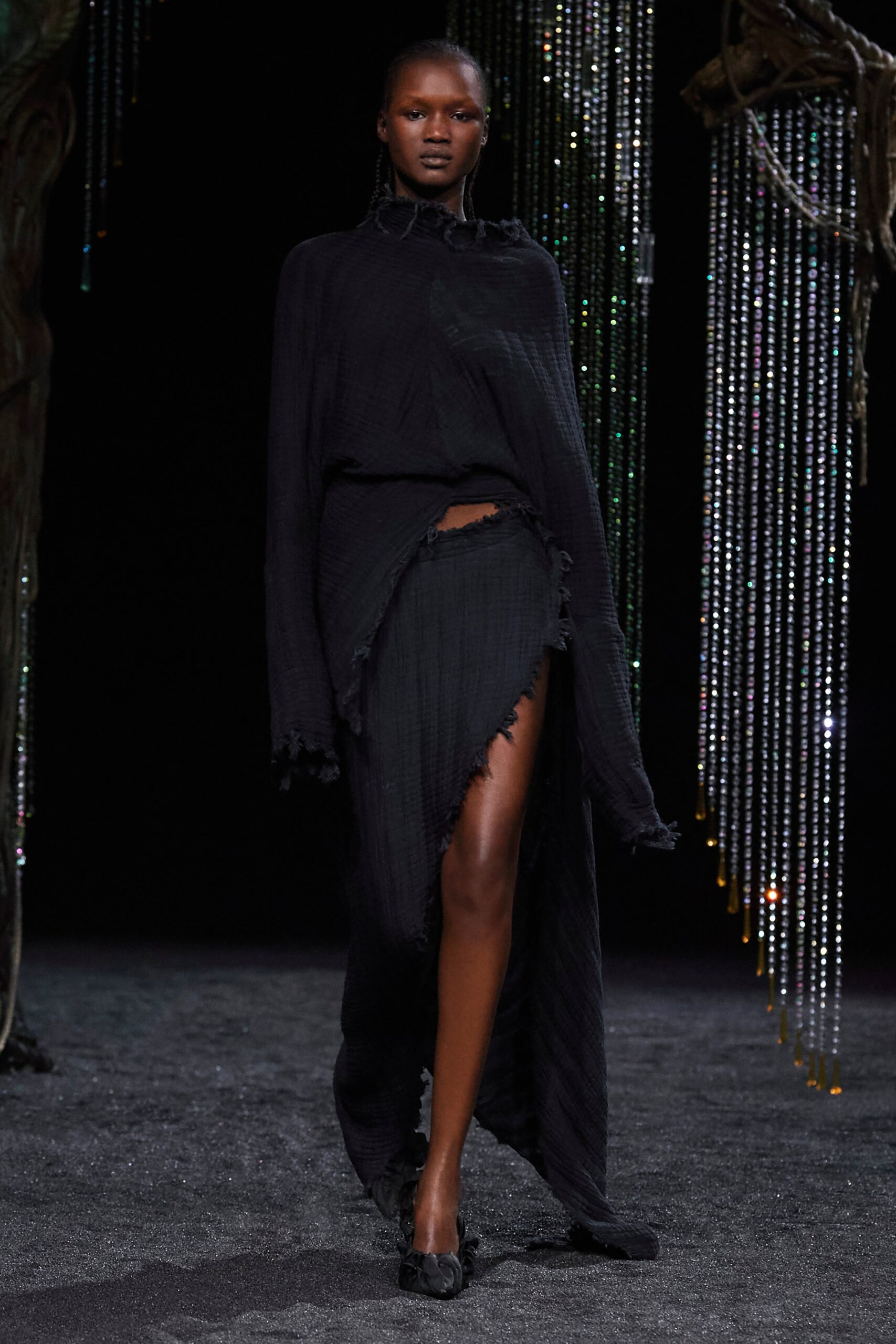 A relaxed black dress with long sleeves, high neckline, and an asymmetric slit detail.