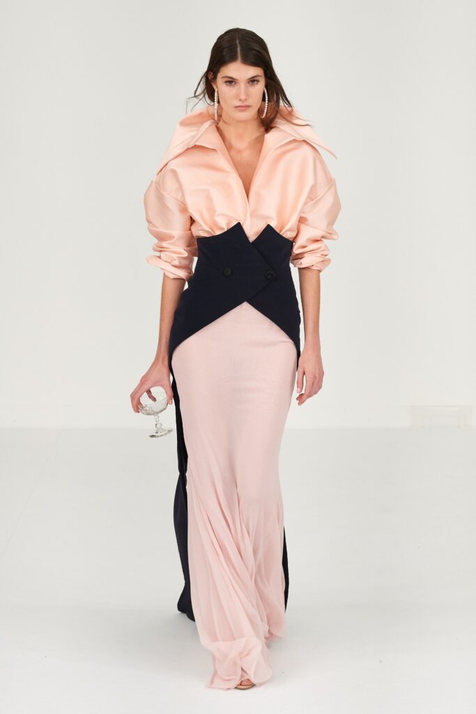 A fitted pink silk dress with a V-neckline, long sleeves, and an asymmetric design.