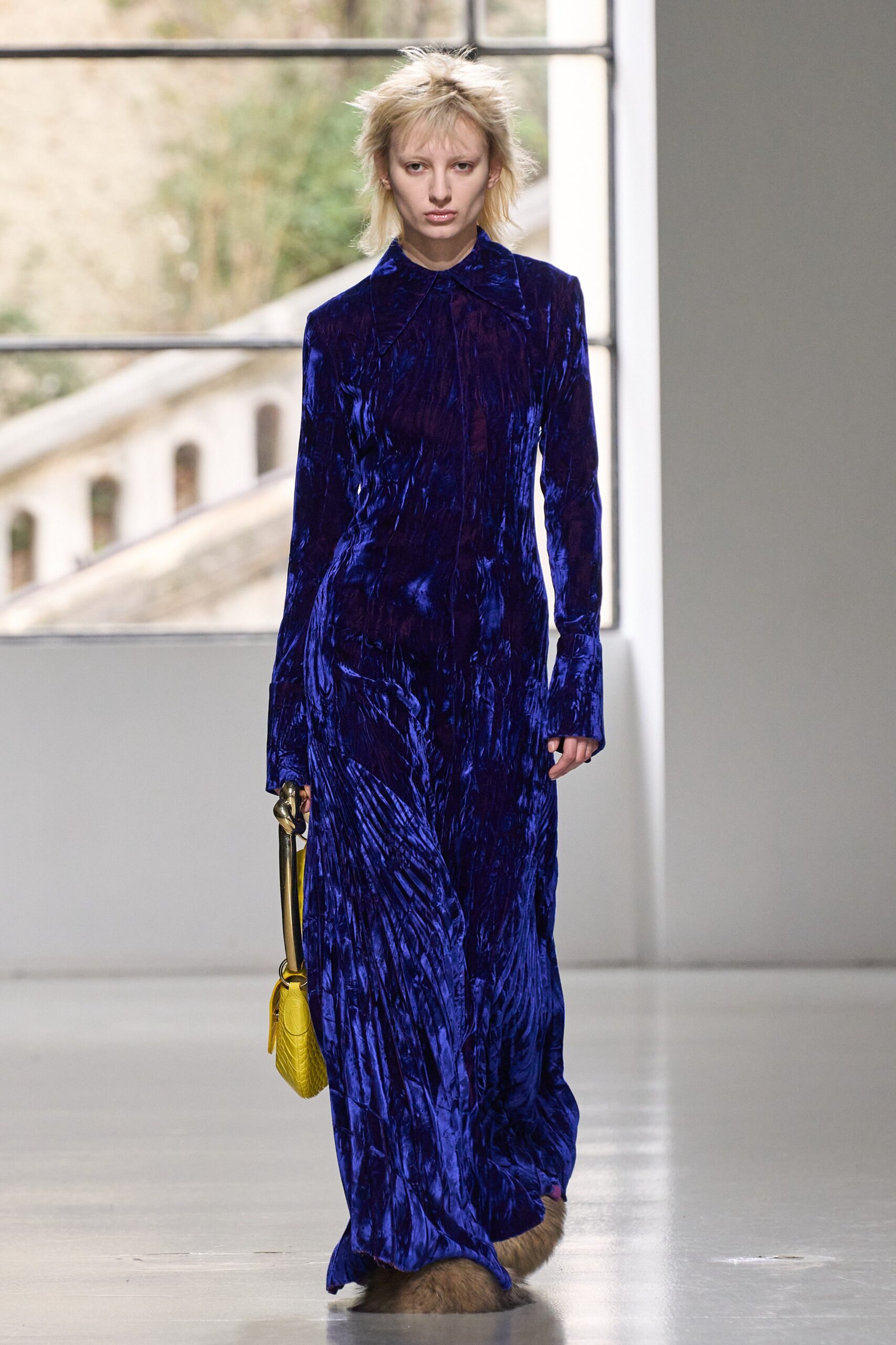 A fitted blue velvet dress with long sleeves and a collared neckline, featuring a draped design.