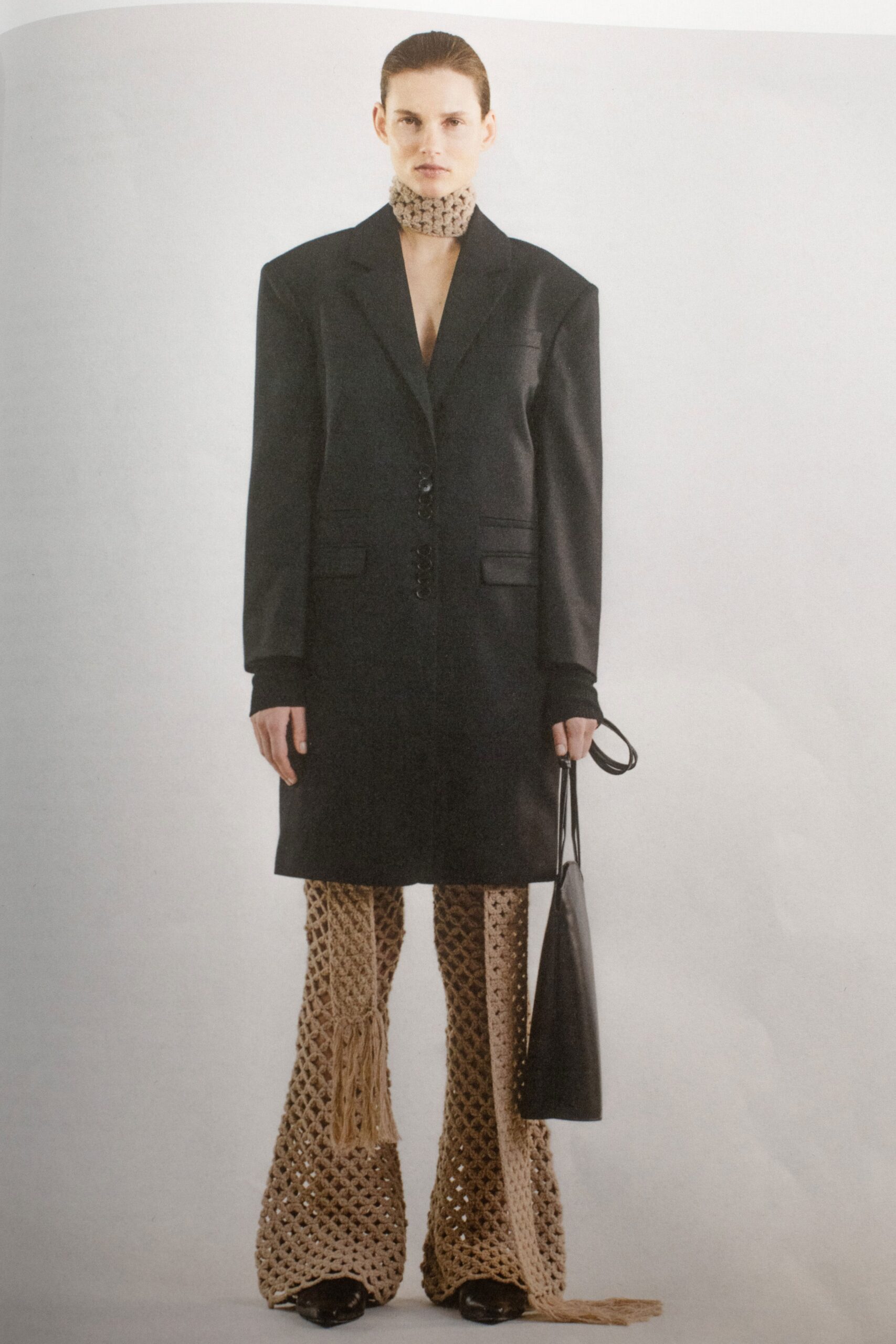 A relaxed black coat paired with fringed wide-leg beige knit pants.