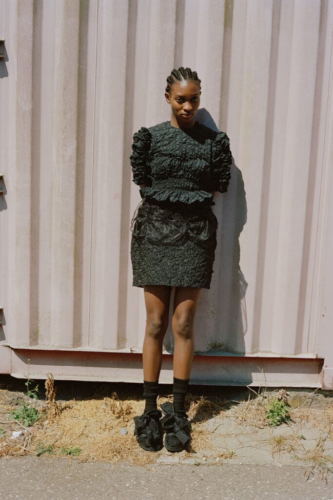 A fitted black dress with ruffled details, short sleeves, and a high neckline.