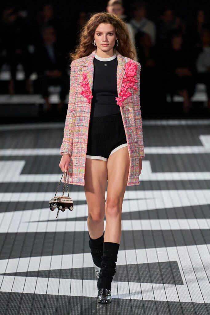 A fitted pink tweed coat layered over a black top with long sleeves and fringed details.
