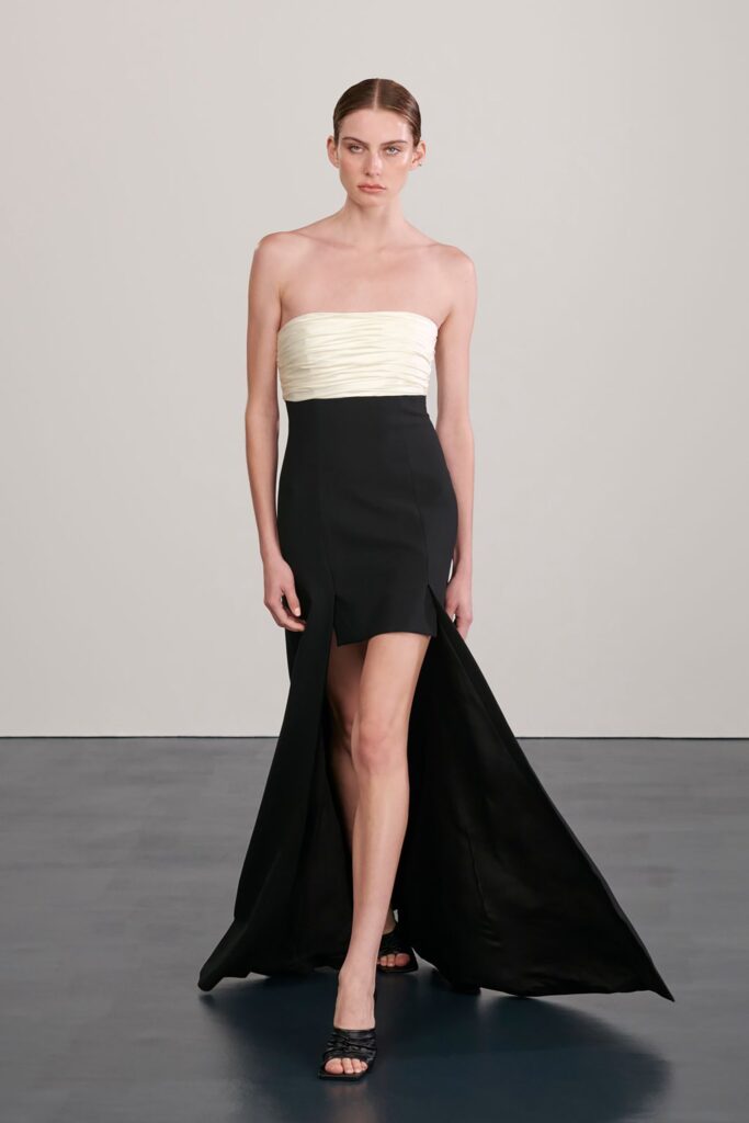 A fitted black and white strapless dress with a V-neckline and a high slit.