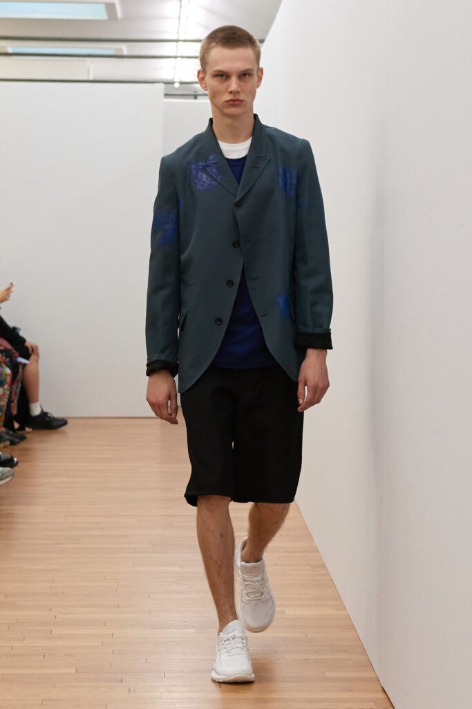 A relaxed blue cotton jacket with a collared neckline paired with black shorts.