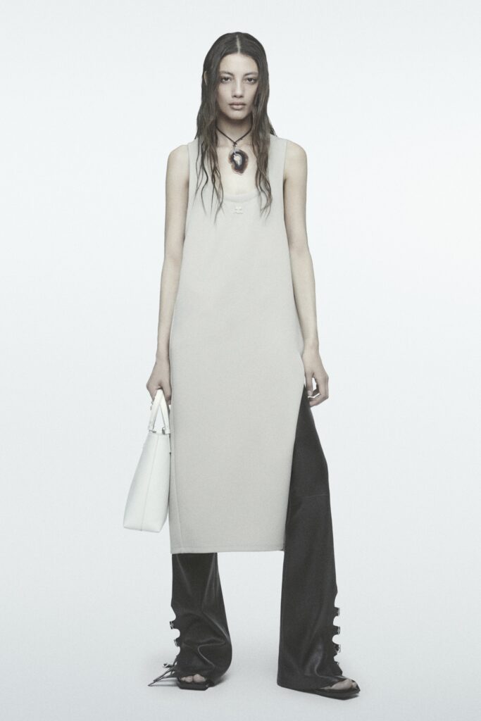A relaxed beige sleeveless dress paired with black straight-leg pants for a modern look.