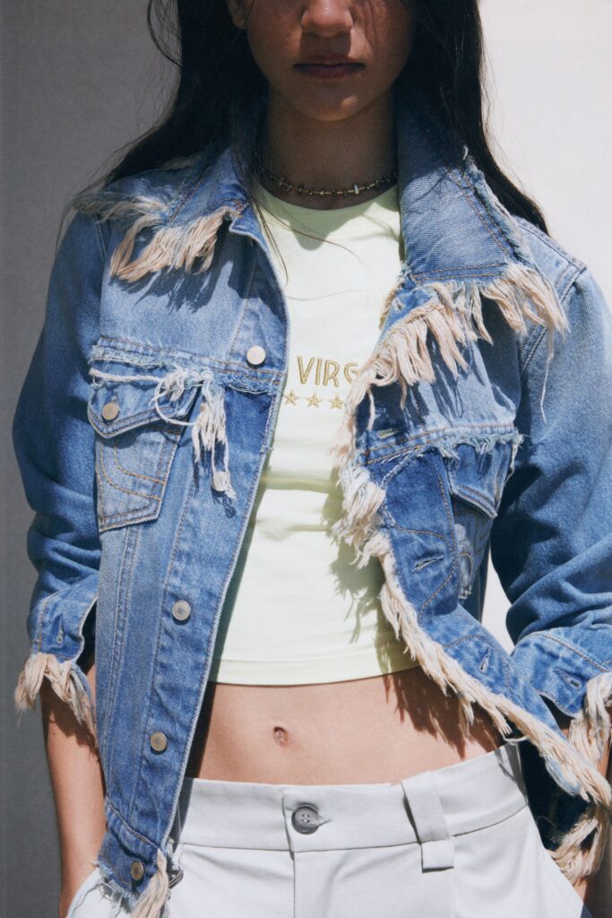 A cropped blue denim jacket with fringed details paired with a green cotton top.