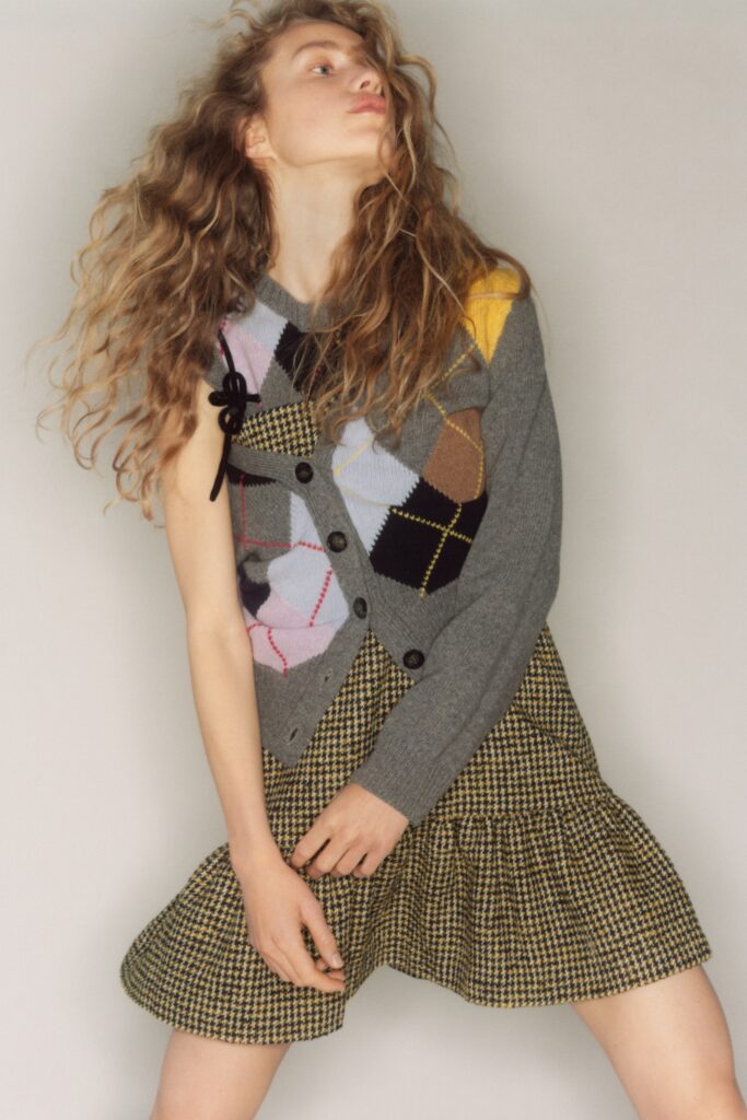 A fitted gray cardigan layered over a pleated dress with a unique pattern.