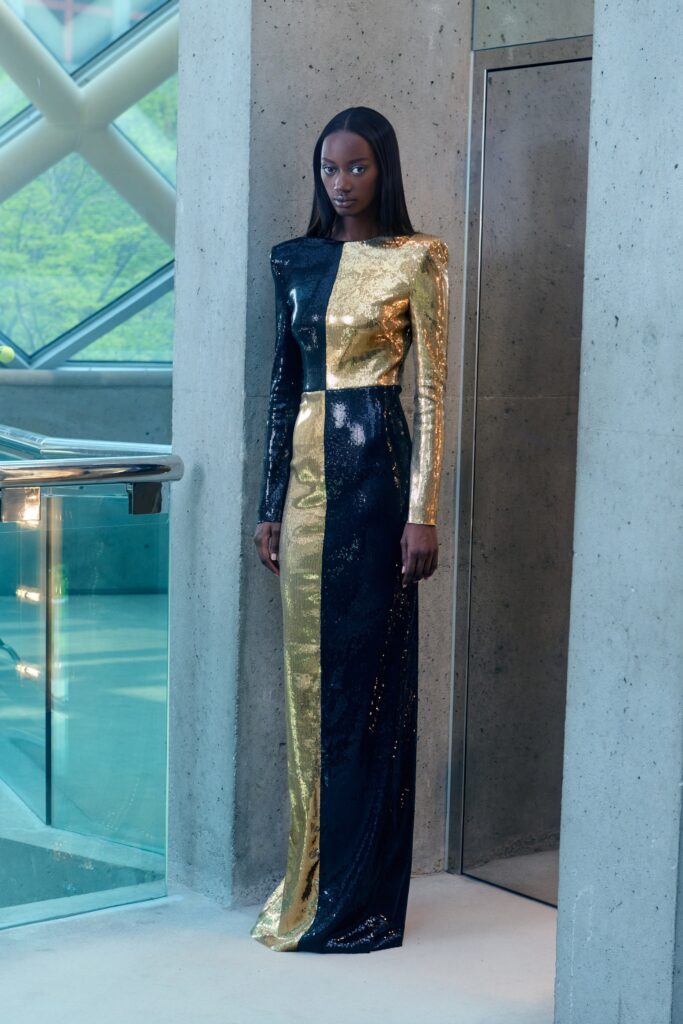 A fitted gown featuring a long-sleeve design with an asymmetric black and gold sequin pattern.