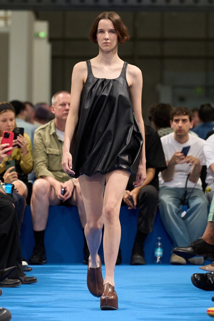 A relaxed black silk sleeveless dress with a high neckline and asymmetric design.