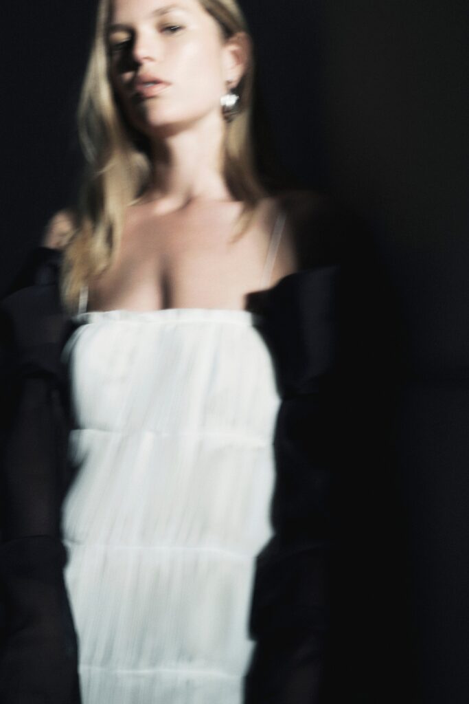 A fitted white silk sleeveless dress with a V-neckline and pleated design.