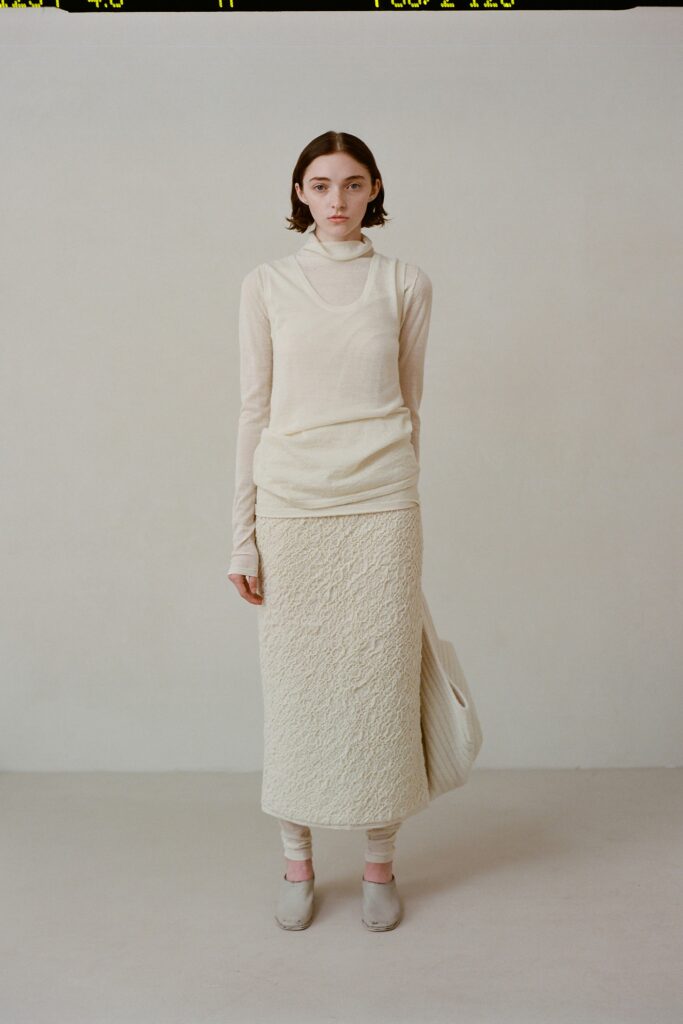 A fitted beige long-sleeve top paired with a textured skirt, creating a layered look.