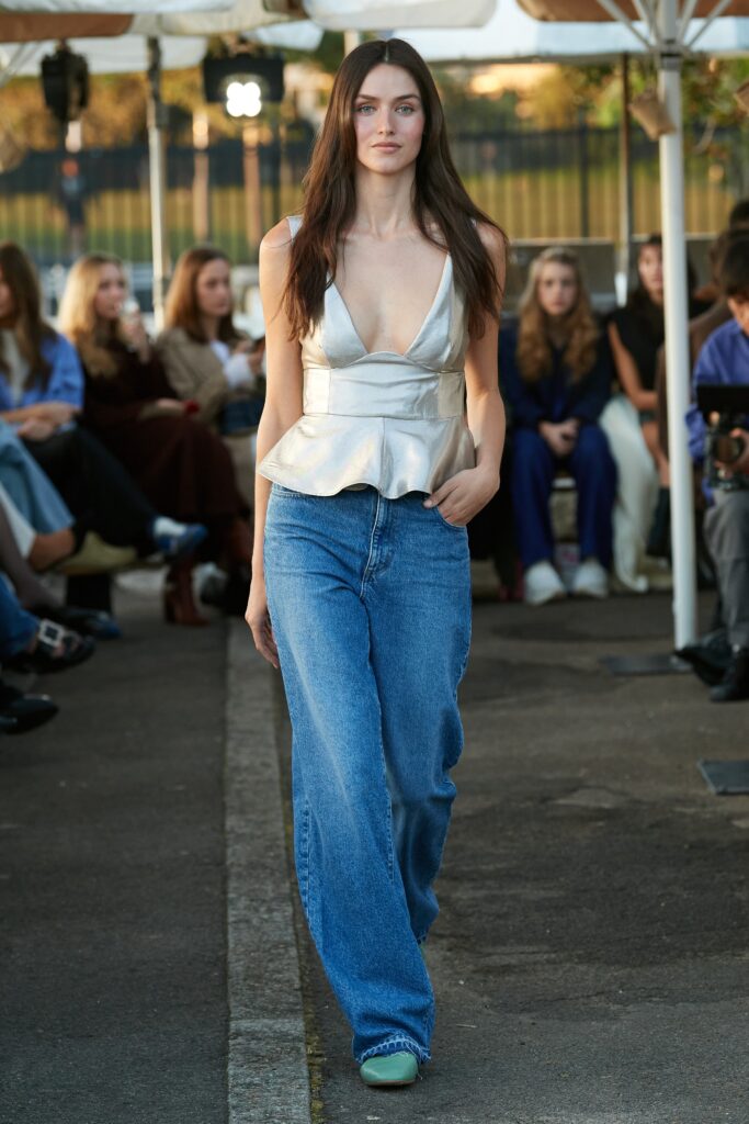 A fitted silver sleeveless top with a V-neckline paired with flared blue denim jeans.