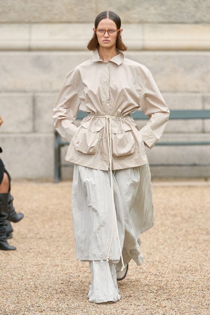 A relaxed beige long-sleeve collared shirt paired with high-waisted pleated gray pants.