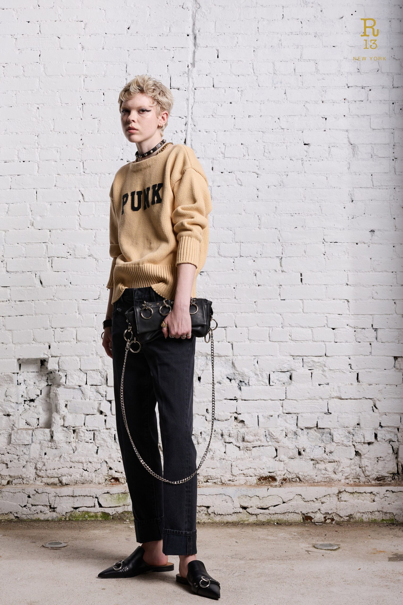 A relaxed beige sweater with printed details paired with straight-leg black denim pants.