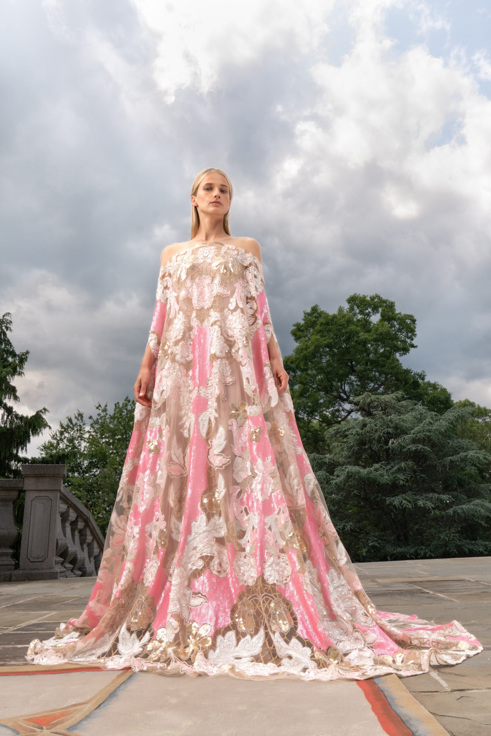 A relaxed pink and beige embroidered gown with an off-shoulder design and layered details.