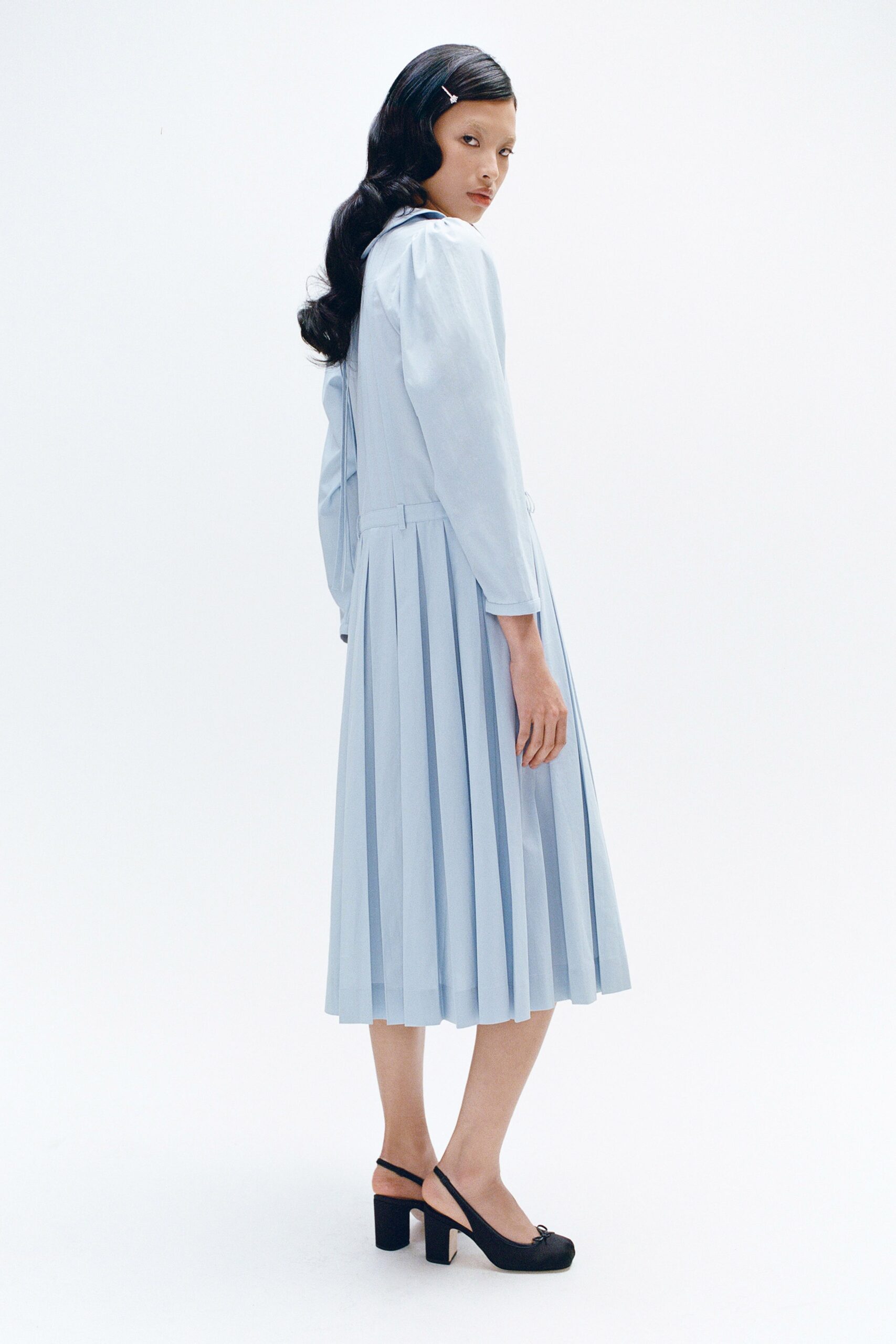A fitted blue cotton long-sleeve dress with pleated details and an A-line silhouette.