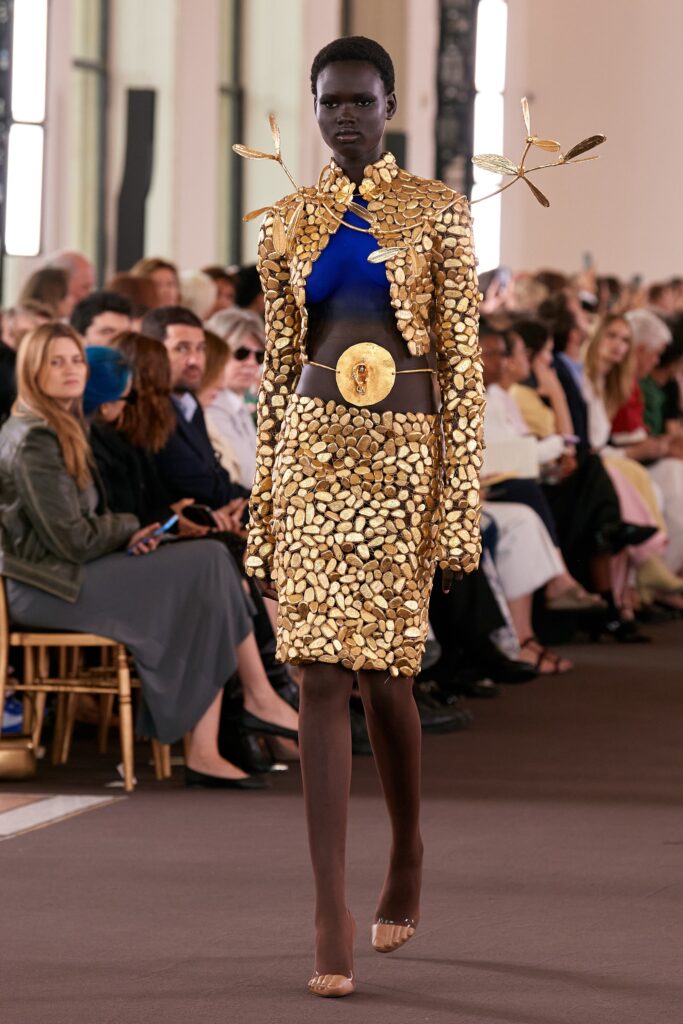 A fitted gold metallic jacket with long sleeves and a collared design paired with a matching skirt.