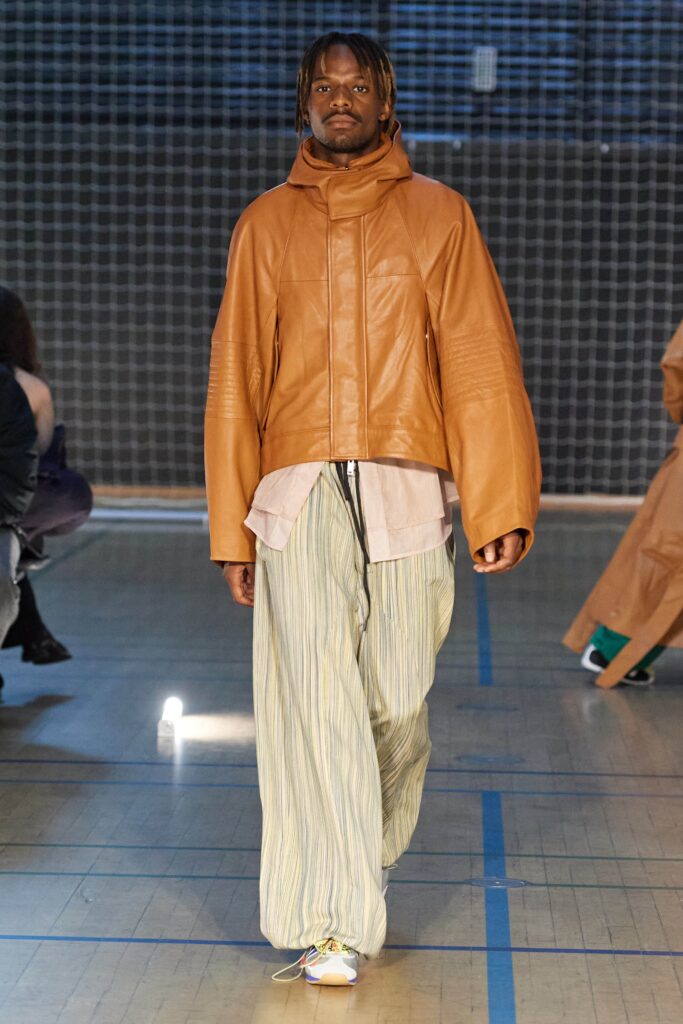 A relaxed brown leather jacket paired with striped cotton pants featuring an asymmetric design.