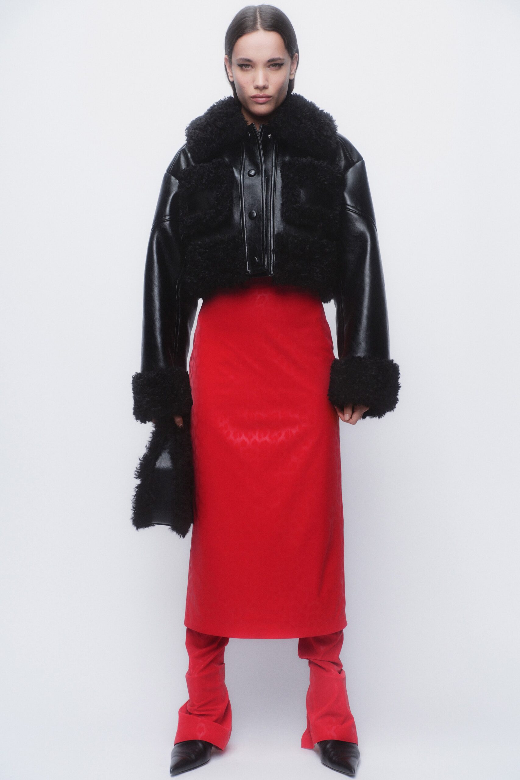 A fitted black leather jacket with a collared neckline paired with a straight-leg red skirt.