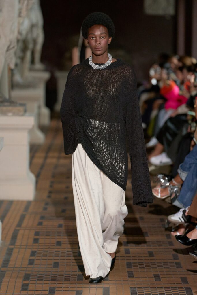A relaxed black long-sleeve top layered over white pants for a chic runway look.