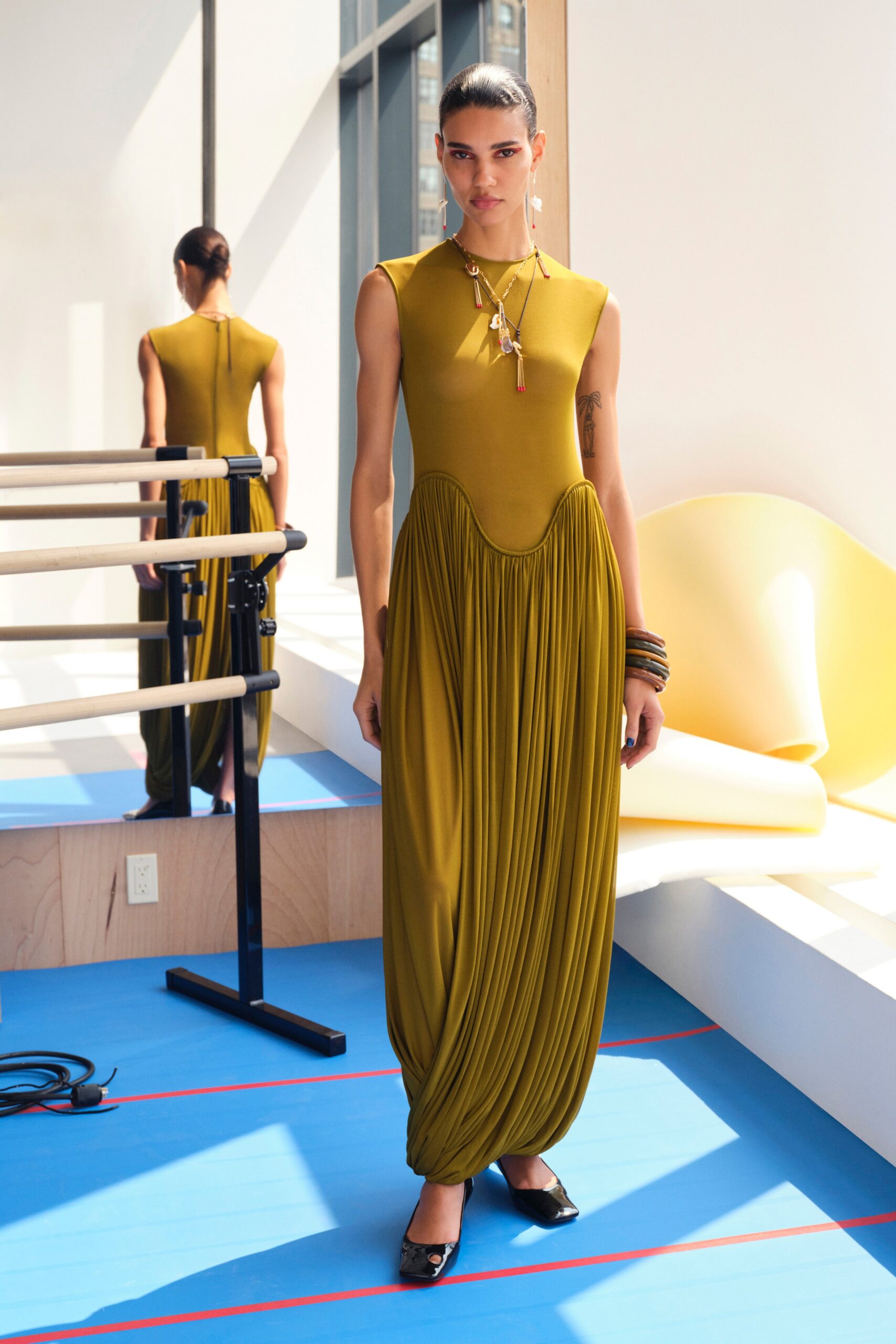 A fitted green sleeveless dress with a high neckline and pleated design.
