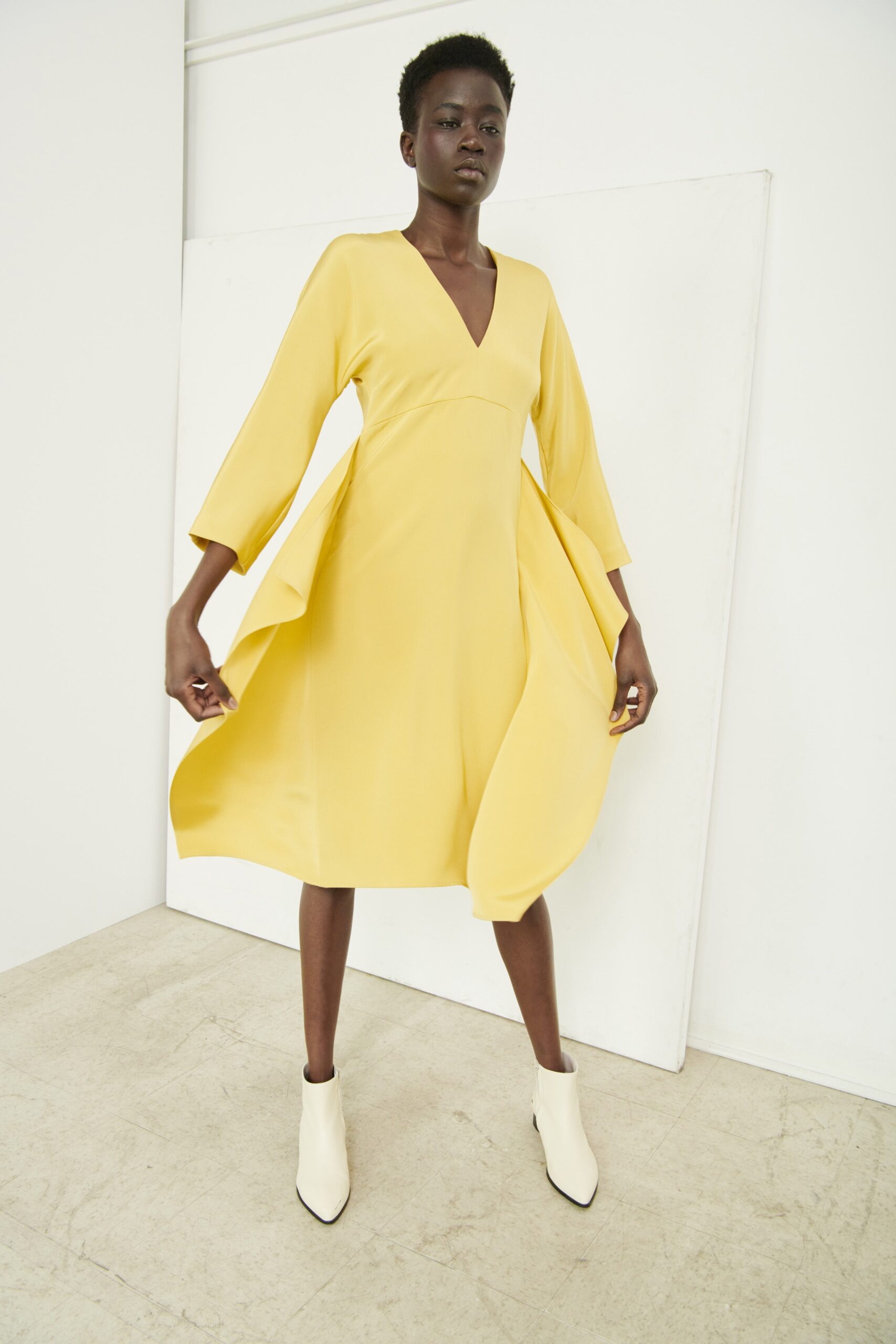 A fitted yellow long-sleeve dress with a V-neckline and pleated A-line silhouette.