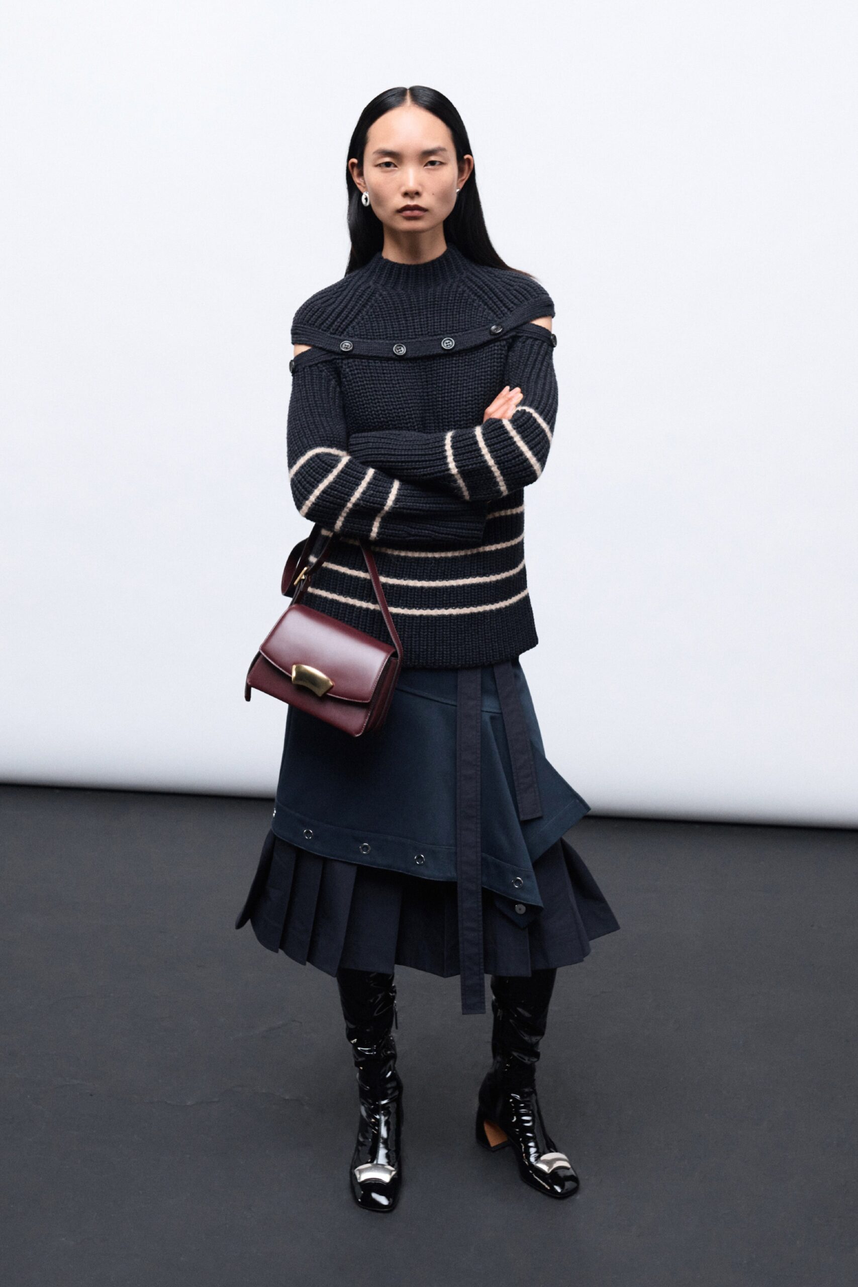 A fitted black wool sweater with an off-shoulder design paired with a layered pleated skirt.